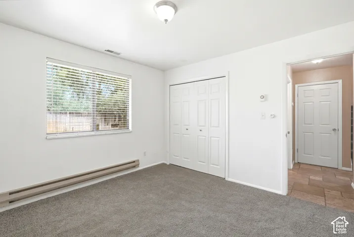 Carpeted room with a large window, bi-fold closet doors, and baseboard heating
