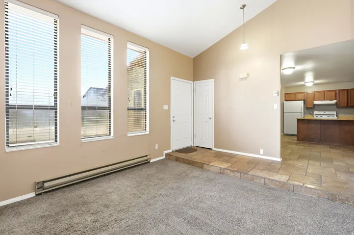 Living area featuring three vertical windows with blinds, a vaulted ceiling with a pendant light fixture, and carpet flooring