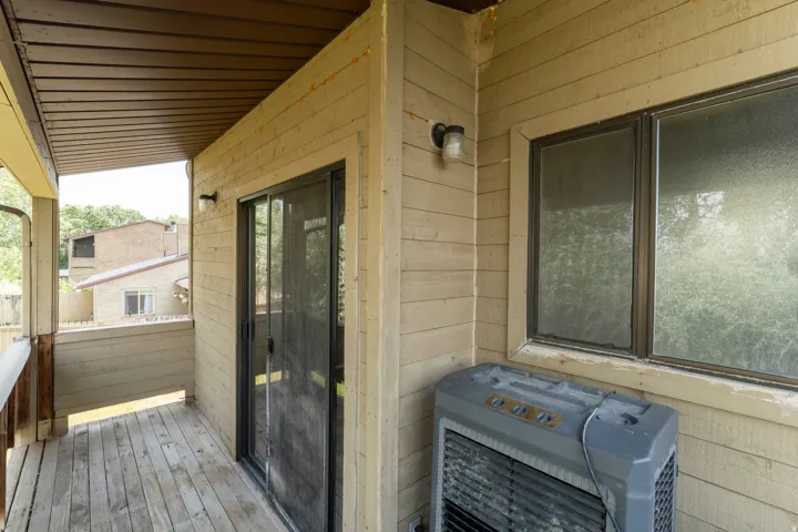 Covered outdoor patio with wood-finish flooring, featuring a sliding glass door and an exterior window