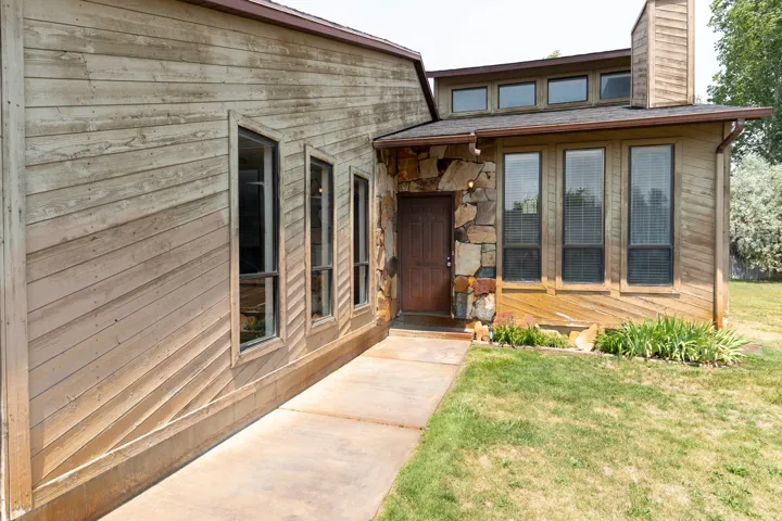 Wood-sided exterior featuring a stone accent wall, multiple vertical windows, upper transom windows, and a prominent wood-paneled chimney