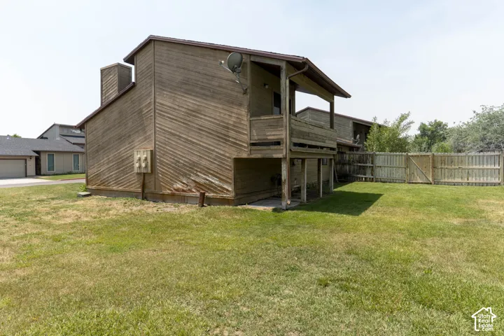 Wood-sided exterior featuring an upper-level balcony, ground-floor patio, and a wood fence enclosing a grassy yard
