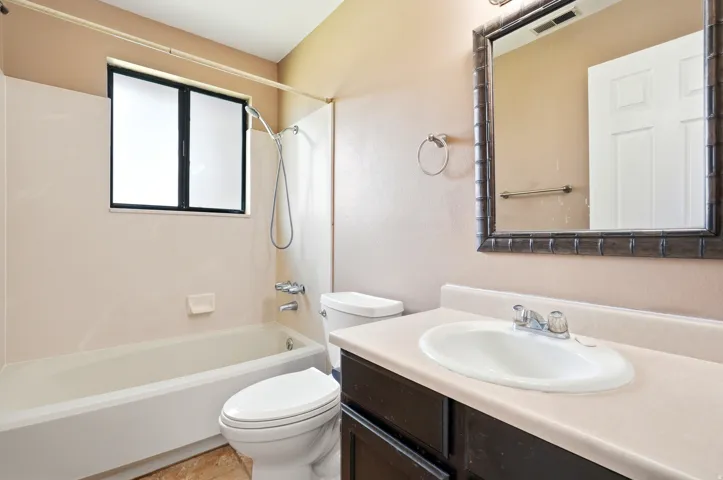 Bathroom featuring a single vanity with a white oval sink, a framed mirror, and a full bathtub with an overhead shower and frosted window