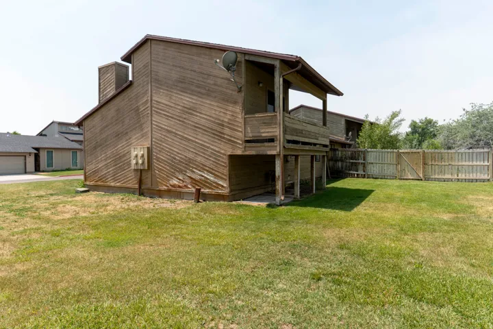 Wood-sided exterior featuring an upper-level balcony, ground-floor patio, and a wood fence enclosing a grassy yard