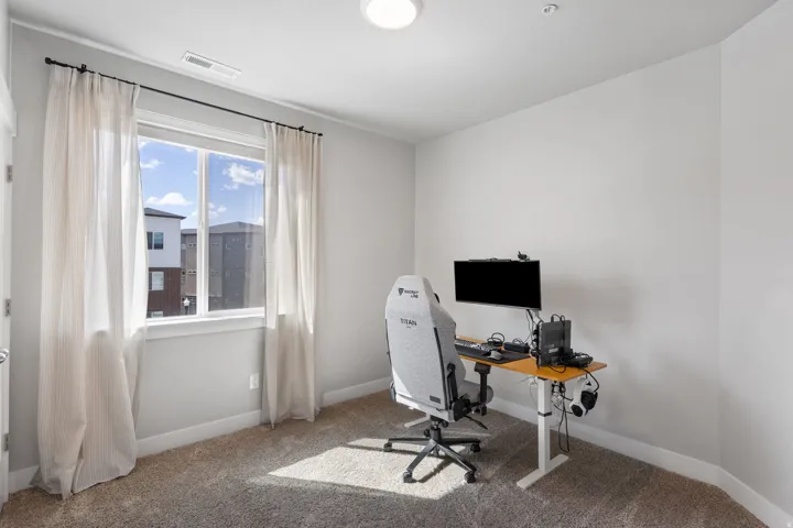 Carpeted interior room featuring a large window with white trim, a ceiling-mounted light fixture, and white baseboards