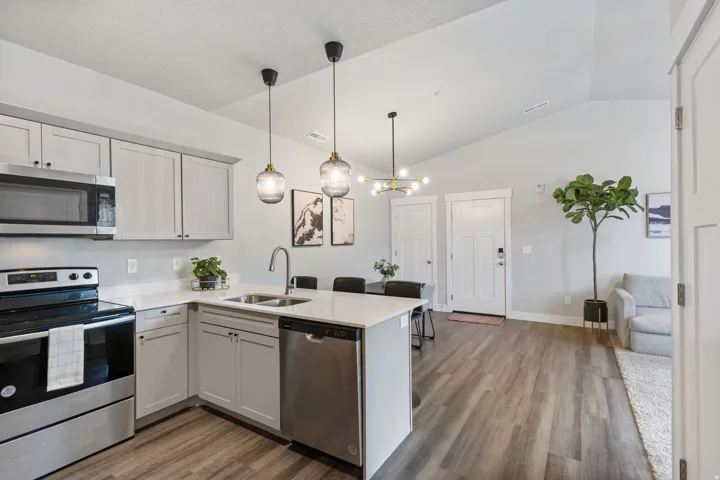Open-concept kitchen and living area featuring wood-finish flooring, vaulted ceilings, and a corner kitchen island with pendant lighting