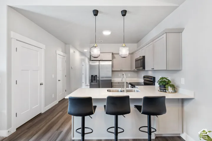 Open-concept kitchen featuring light-toned cabinetry, stainless steel appliances, and a central island with a sink