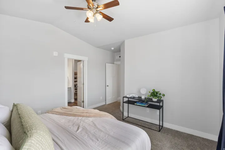 Spacious room featuring vaulted ceilings, a ceiling fan with integrated lighting, neutral wall tones, and plush carpet flooring
