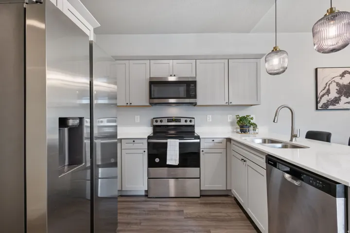 Modern kitchen featuring stainless steel appliances, light gray cabinetry, crisp white countertops, a stainless steel sink with a gooseneck faucet, and wood-finish flooring