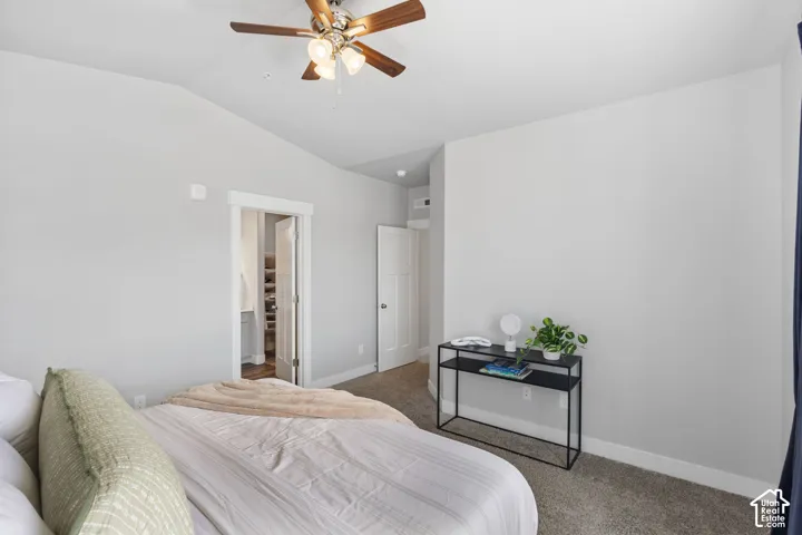 Spacious room featuring vaulted ceilings, a ceiling fan with integrated lighting, neutral wall tones, and plush carpet flooring