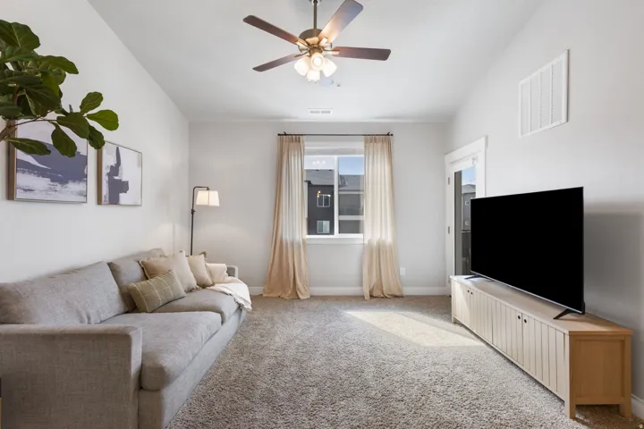 Carpeted interior space featuring a ceiling fan with integrated lighting, a window with natural light, and a white door with glass panels