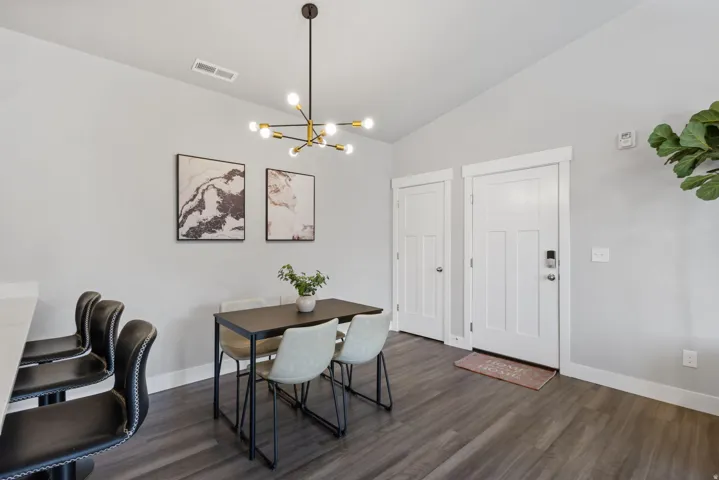 Open-concept dining area featuring vaulted ceilings, wood-finish flooring, and a modern chandelier