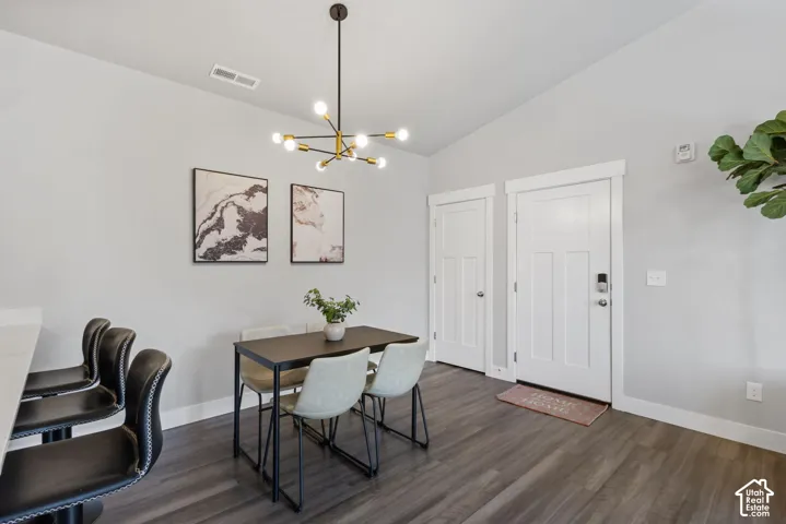 Open-concept dining area featuring vaulted ceilings, wood-finish flooring, and a modern chandelier