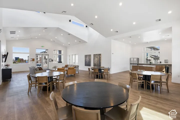 Spacious common area featuring vaulted ceilings, recessed lighting, wood-finish flooring, a full kitchen with stainless steel appliances, and large windows