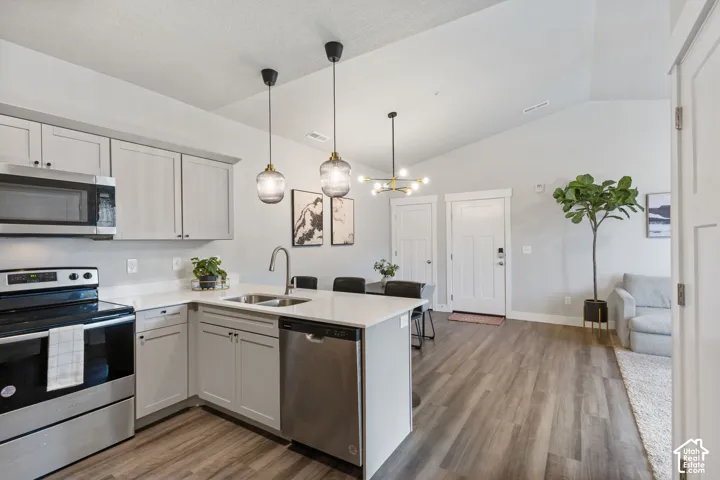 Open-concept kitchen and living area featuring wood-finish flooring, vaulted ceilings, and a corner kitchen island with pendant lighting