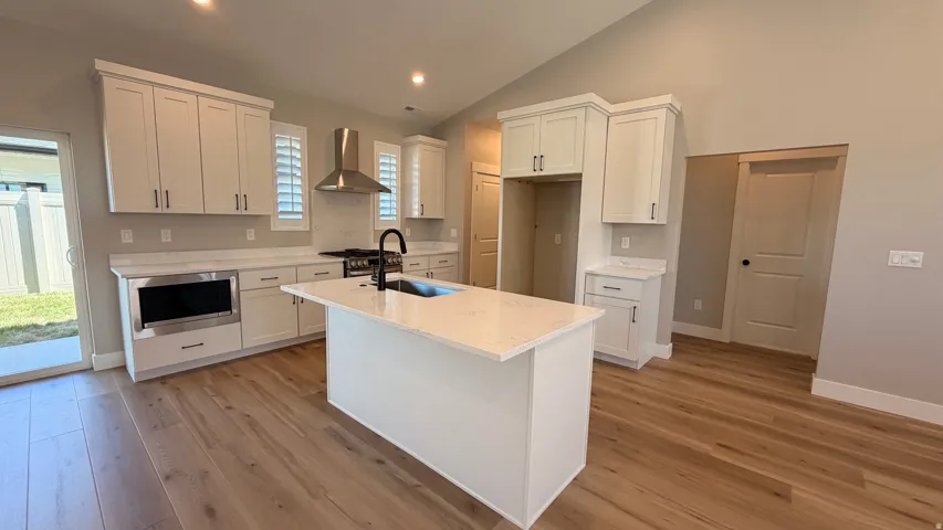 Spacious kitchen featuring an island, light wood-finish flooring, white cabinetry, a built-in microwave, and a stainless steel range hood