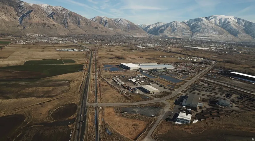 Expansive aerial landscape featuring a highway, commercial structures, and a residential area with snow-capped mountains in the background