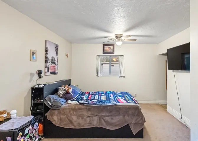 Carpeted interior room featuring a window with a built-in air conditioning unit, a ceiling fan with integrated lighting, and light-colored walls