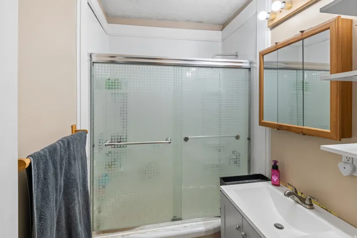 Bathroom featuring a shower with patterned frosted glass sliding doors, a vanity with an integrated white sink, brushed nickel faucet, and a wall-mounted mirrored medicine cabinet with wood-finish trim