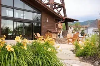 Exterior featuring a large wall of windows, an adjacent sliding glass door, natural wood siding, and a covered patio area with stone pavers