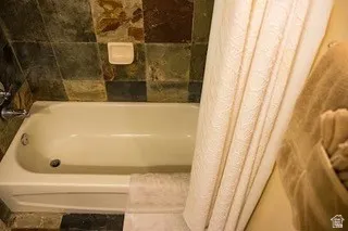 Alcove bathtub with a neutral finish, surrounded by variegated stone-finish wall tile and coordinating floor tile