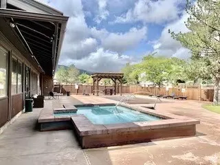 Outdoor aquatic area featuring a swimming pool with an integrated hot tub, extensive concrete patio, and a wooden pergola structure