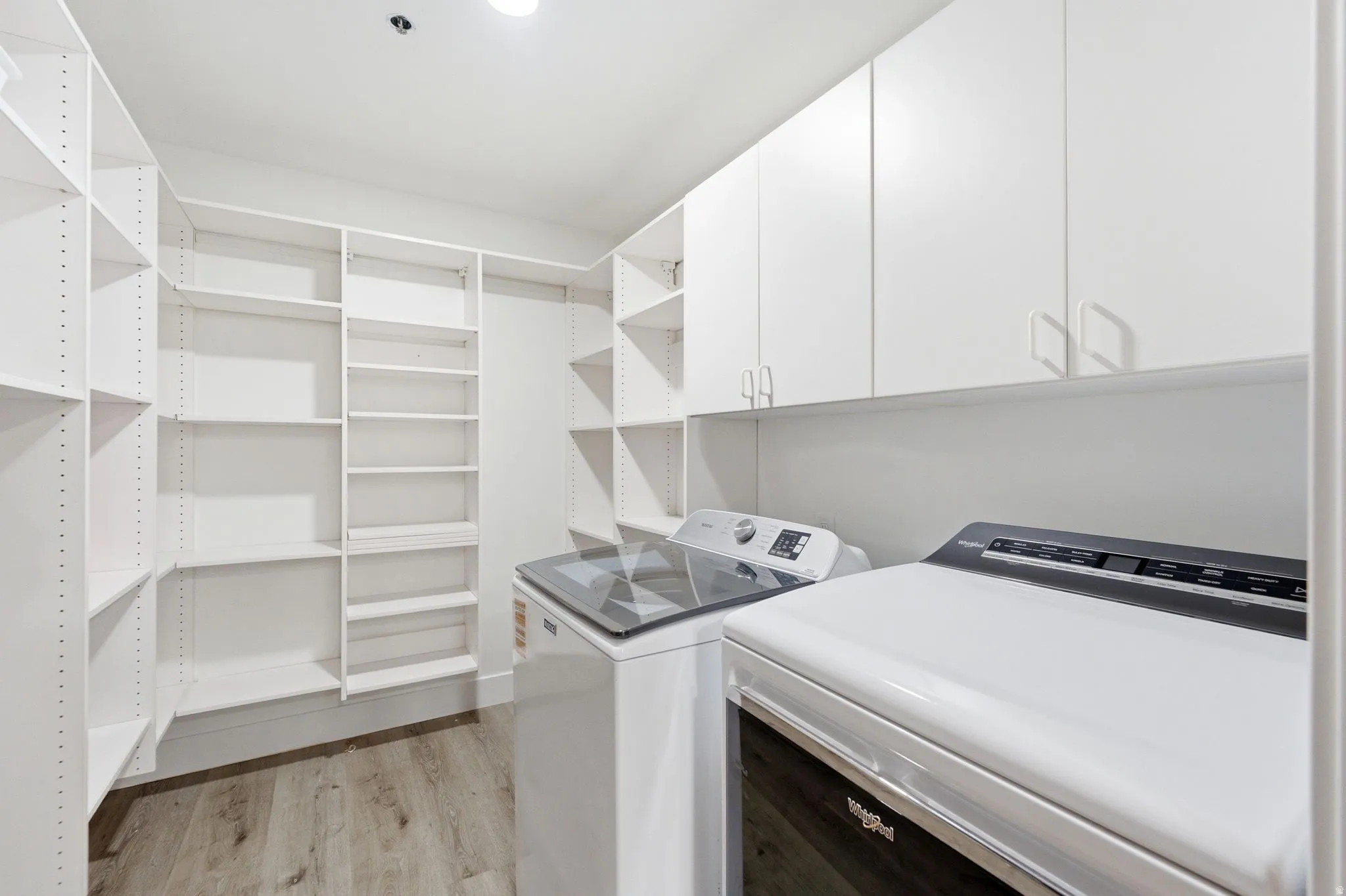 Dedicated laundry area featuring white upper cabinetry and wood-finish flooring
