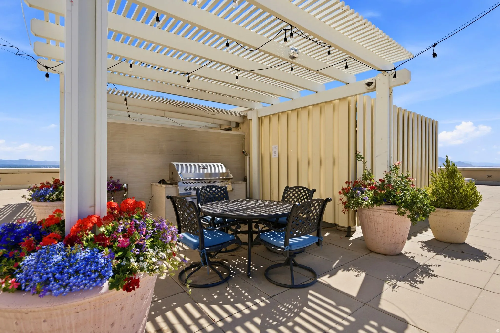 Rooftop patio featuring a white slatted pergola, integrated string lighting, and a built-in stainless steel grill