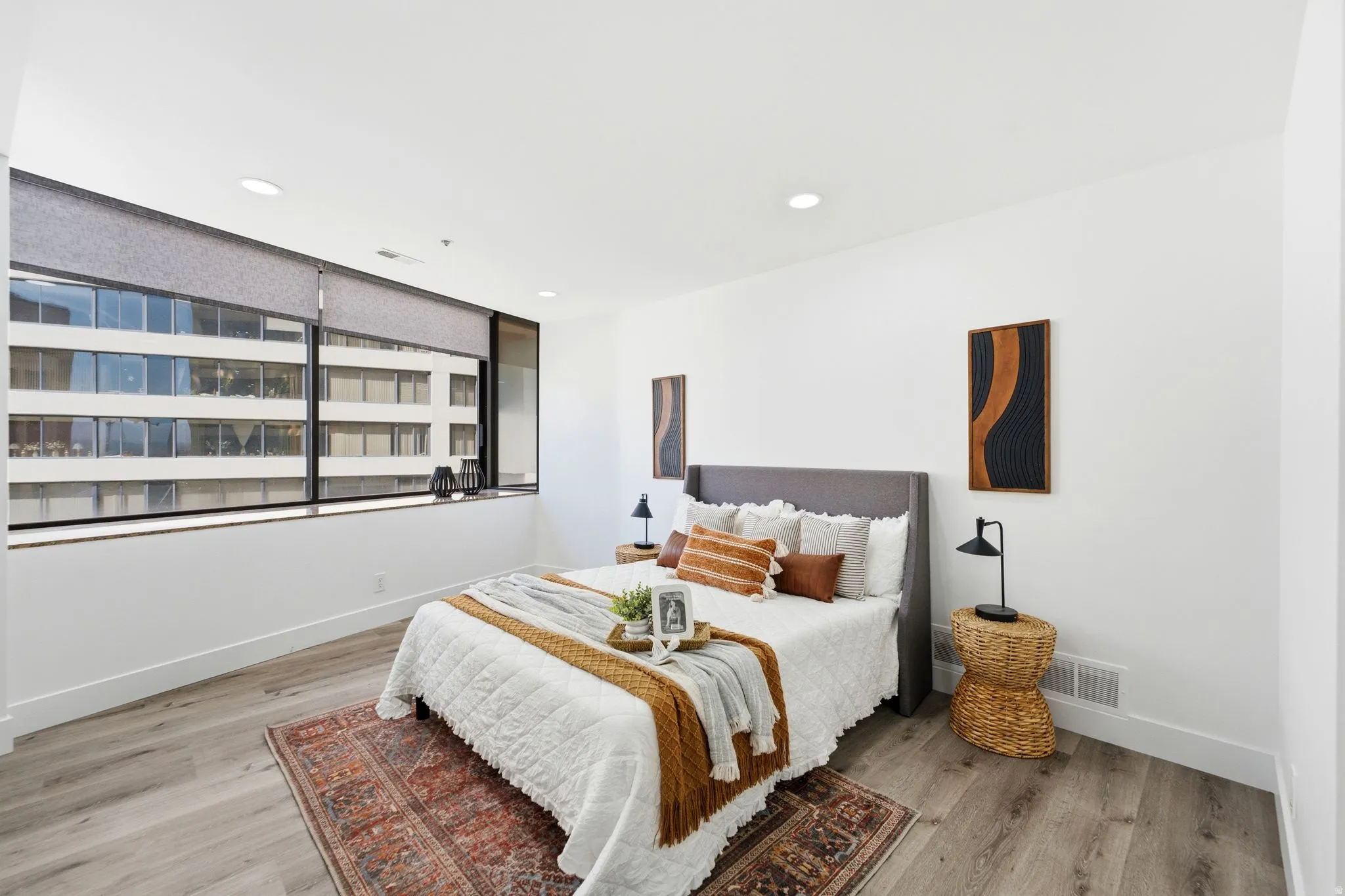 Spacious Master bedroom featuring a wall of windows with roller shades, wood-finish flooring, recessed lighting, and crisp white walls