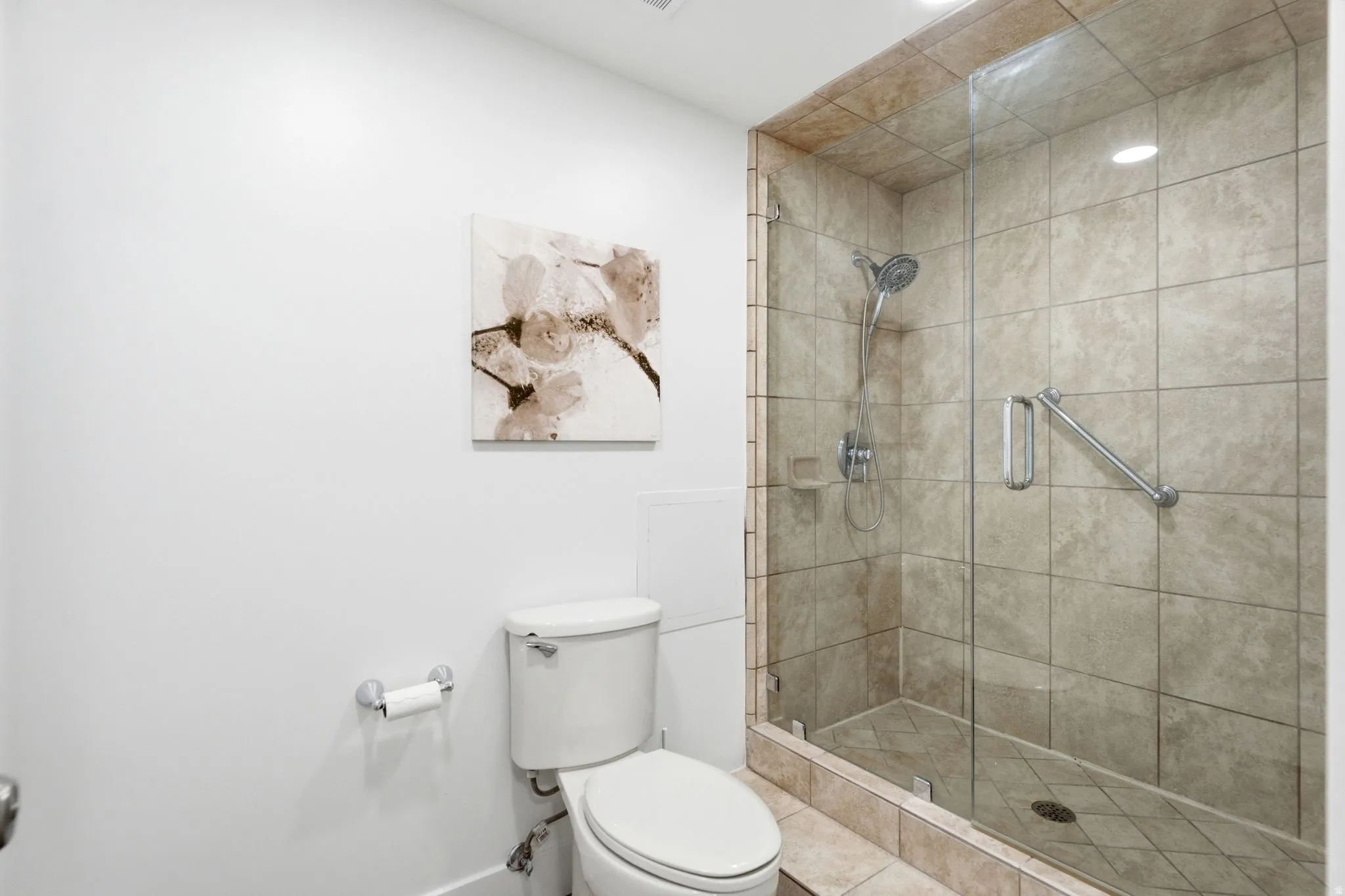 Glass-enclosed master shower with tiled walls and floor, featuring a multi-function showerhead and grab bar