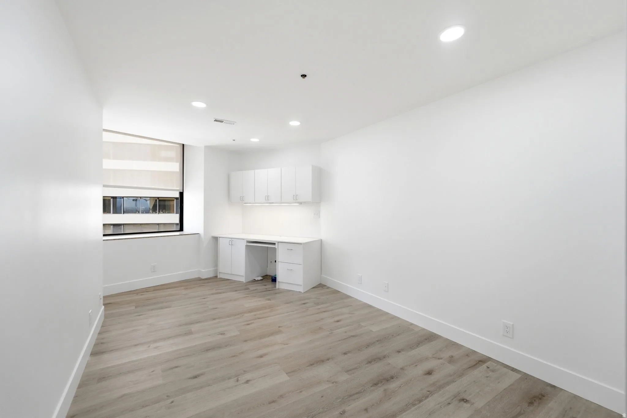 Second bedoom featuring wood-finish flooring, recessed lighting, and a built-in desk with white cabinetry