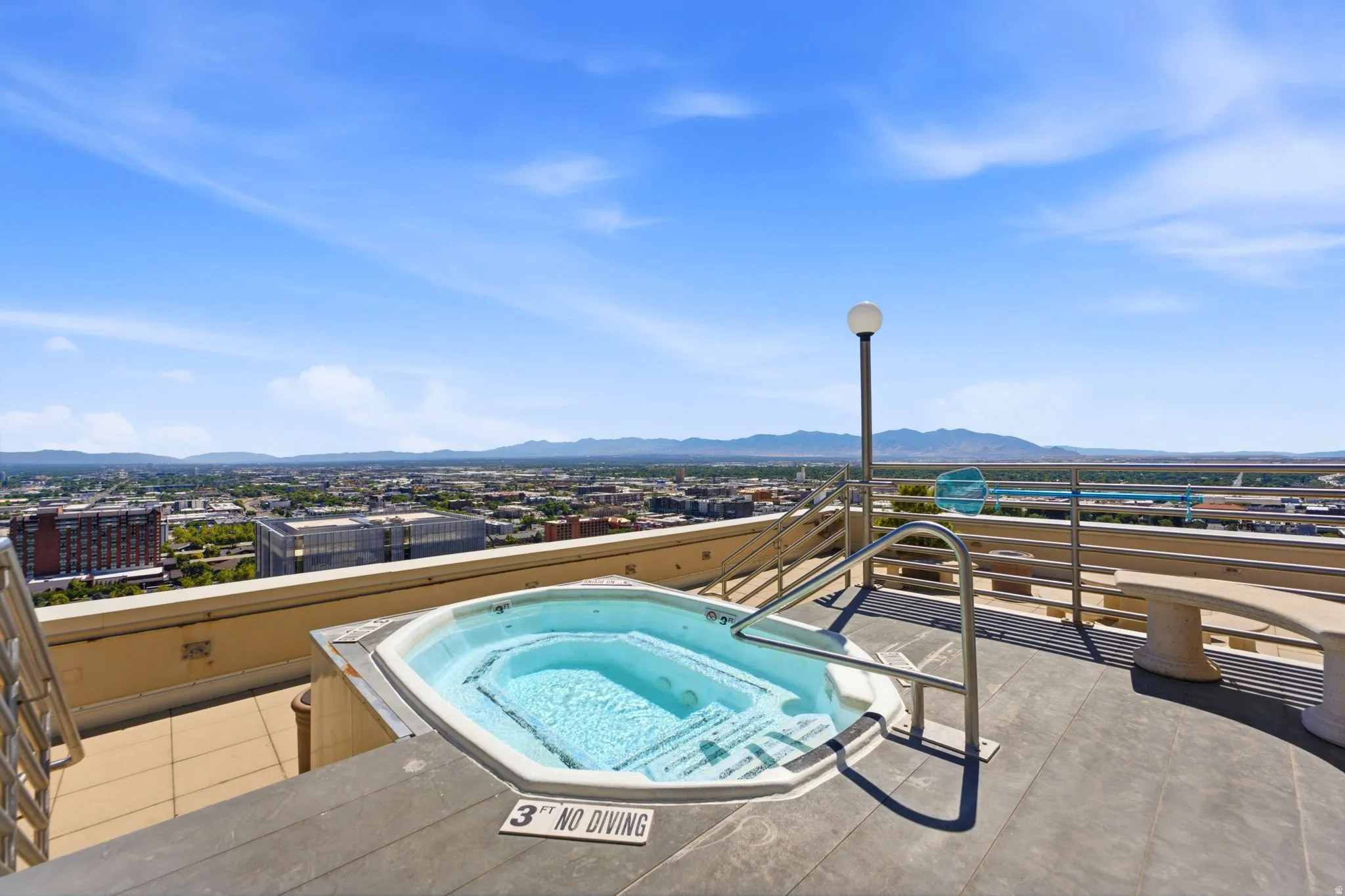 Rooftop hot tub with metal handrails, surrounded by composite decking and a concrete retaining wall
