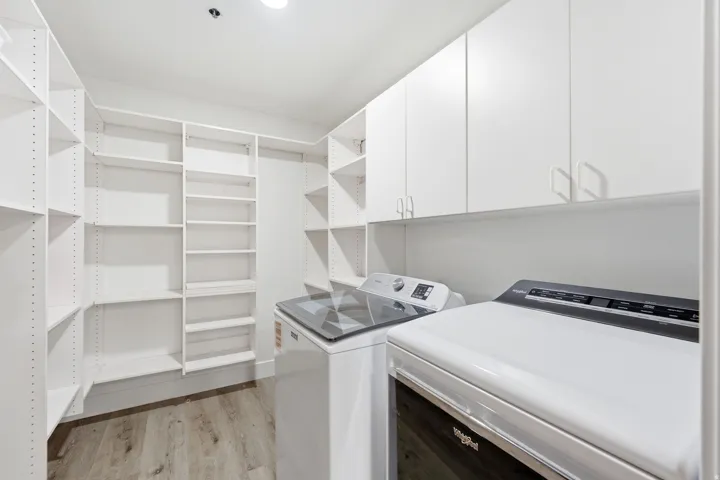 Dedicated laundry area featuring white upper cabinetry and wood-finish flooring