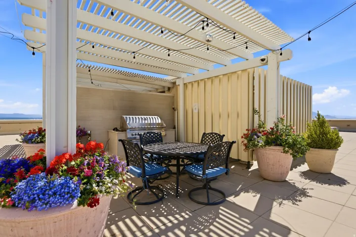 Rooftop patio featuring a white slatted pergola, integrated string lighting, and a built-in stainless steel grill