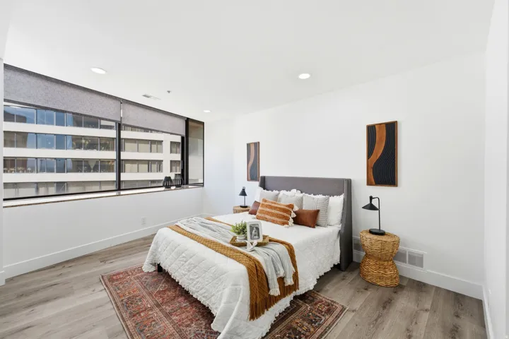 Spacious Master bedroom featuring a wall of windows with roller shades, wood-finish flooring, recessed lighting, and crisp white walls