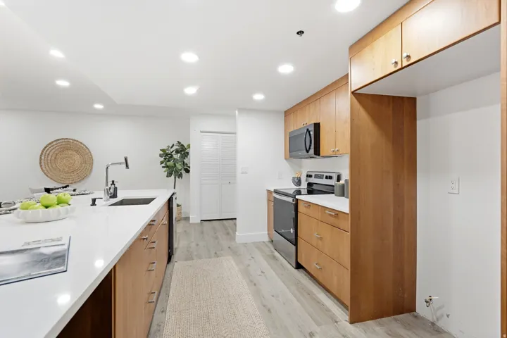 Kitchen featuring light wood-finish cabinetry, white countertops, built-in stainless-steel appliances, a kitchen island with an undermount sink and matte black faucet, and wood-finish flooring