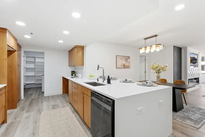 Contemporary kitchen featuring wood cabinetry, light-toned flooring, and a spacious center island with an integrated sink and dishwasher