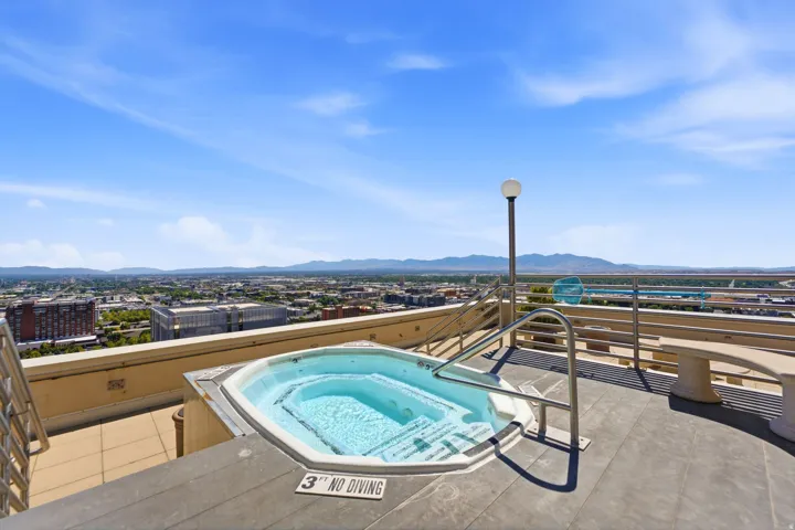 Rooftop hot tub with metal handrails, surrounded by composite decking and a concrete retaining wall