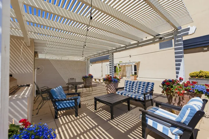 Spacious patio area featuring a slatted pergola, string lighting, an outdoor counter, and a concrete paver surface