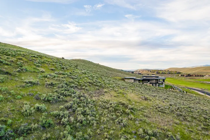 Modern residence featuring stone and dark siding, set into a natural hillside with expansive green spaces