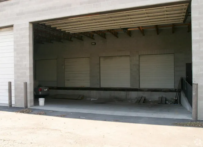 Industrial loading dock featuring three roll-up doors, a concrete block exterior, and an open bay area with exposed beam ceiling