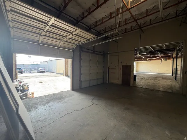Industrial warehouse space featuring concrete flooring, exposed ceiling rafters, and a large roll-up door