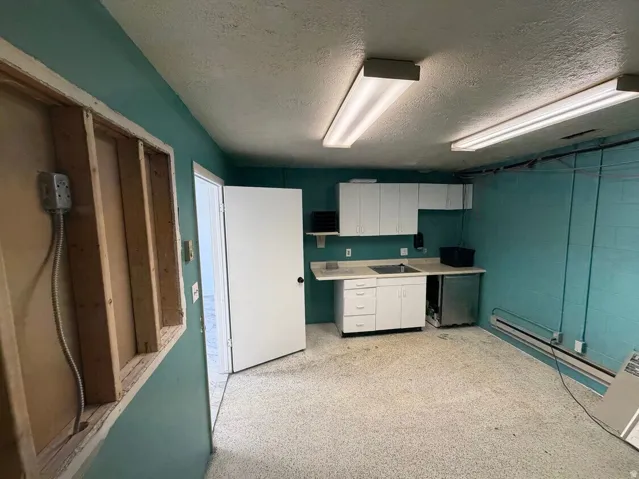 Functional utility area featuring a sink with white cabinetry, fluorescent ceiling lights, and speckled flooring