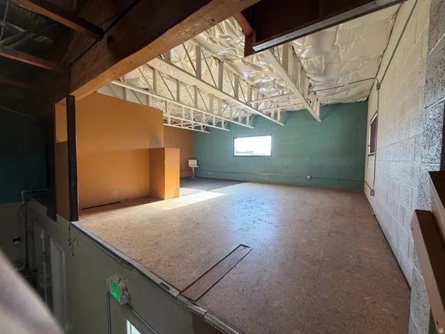 Open mezzanine level with exposed wood beams, cork-finish flooring, and industrial-style ceiling trusses