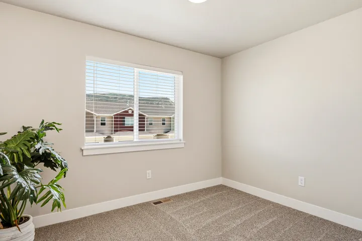 Neutral-toned interior room featuring a window with white blinds, light beige walls, and tan carpet flooring