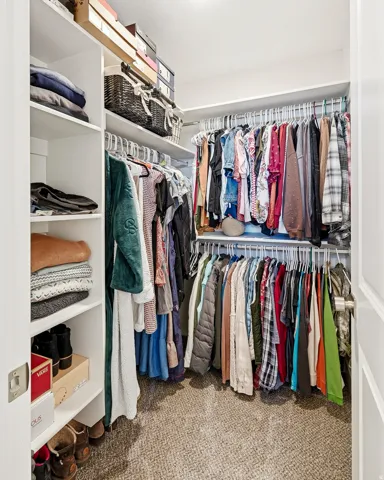 Walk-in closet featuring built-in shelving, multiple hanging rods, corner configuration, and carpeted flooring