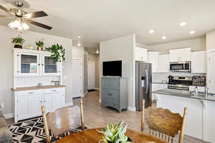 Open-concept living space featuring wood-finish flooring throughout, a ceiling fan with integrated lighting, recessed ceiling lights, a kitchen with white cabinetry, and stainless steel appliances