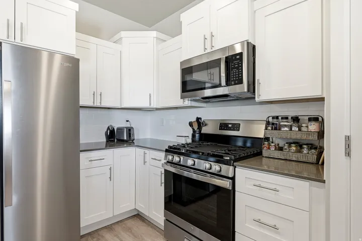 Contemporary kitchen featuring white shaker cabinetry with brushed nickel hardware, stainless steel appliances, a subway tile backsplash, dark countertops, and wood-finish flooring