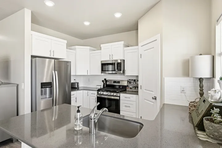 Kitchen featuring a spacious island with an undermount sink, stainless steel appliances, white shaker cabinetry, light-toned countertops, and a white subway tile backsplash