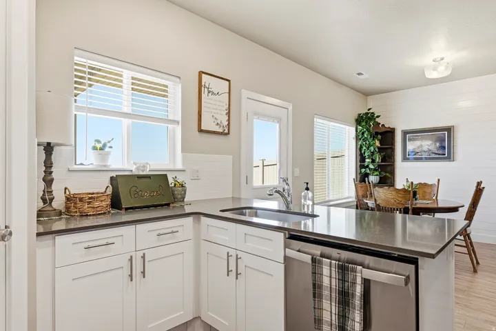Kitchen featuring white cabinetry, dark countertops, a stainless steel sink, and a built-in dishwasher