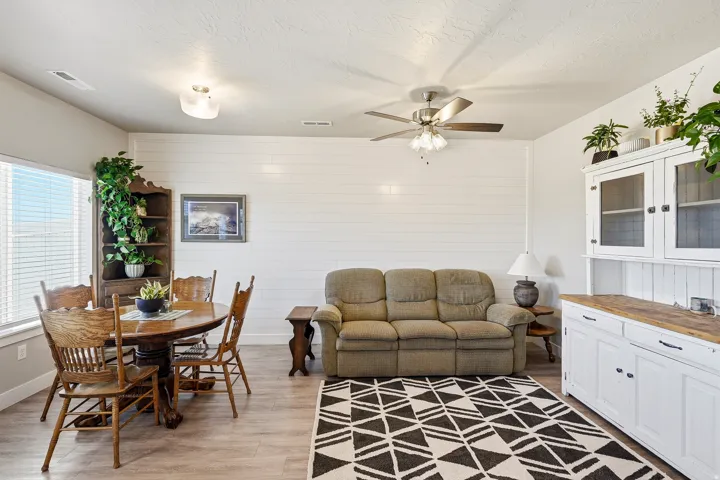 Open-concept living space featuring wood-finish flooring, white shiplap accent wall, and a ceiling fan with integrated lighting